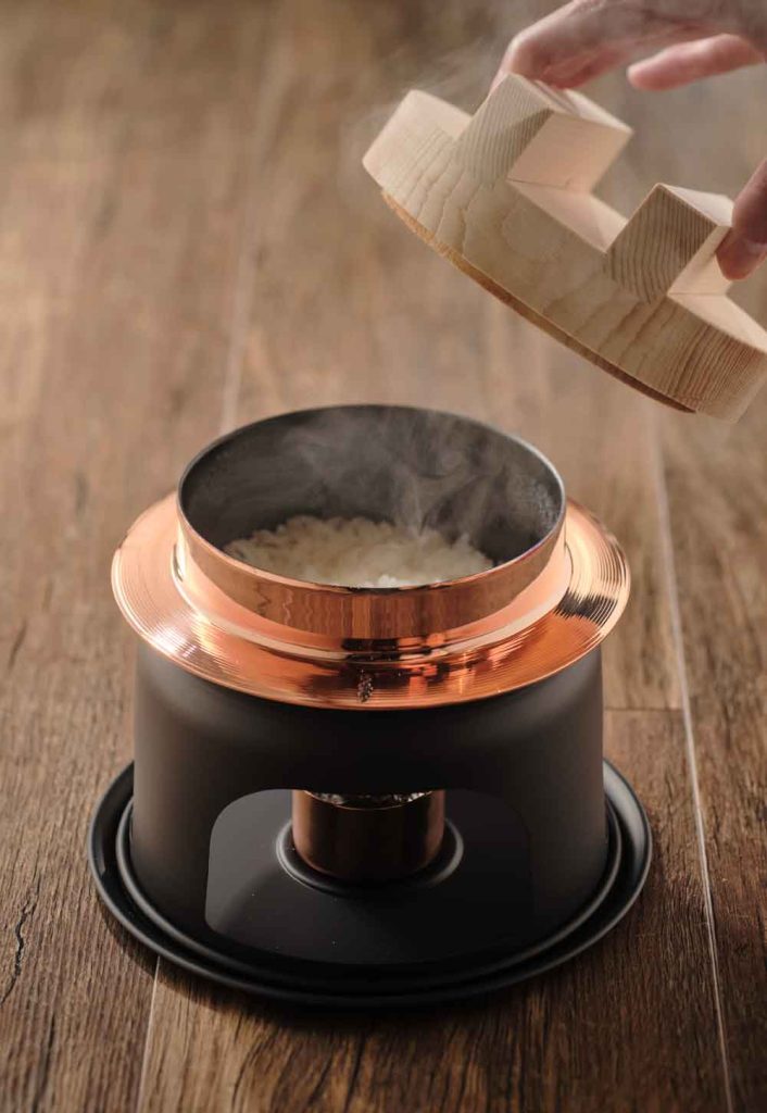 炊きたての白いご飯が入った銅釜の木蓋を開けている様子