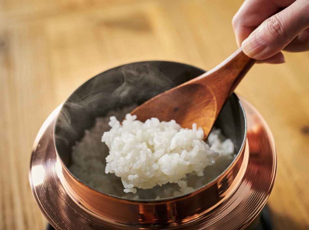 銅釜で炊いた炊きたてのご飯を木製しゃもじですくっている様子